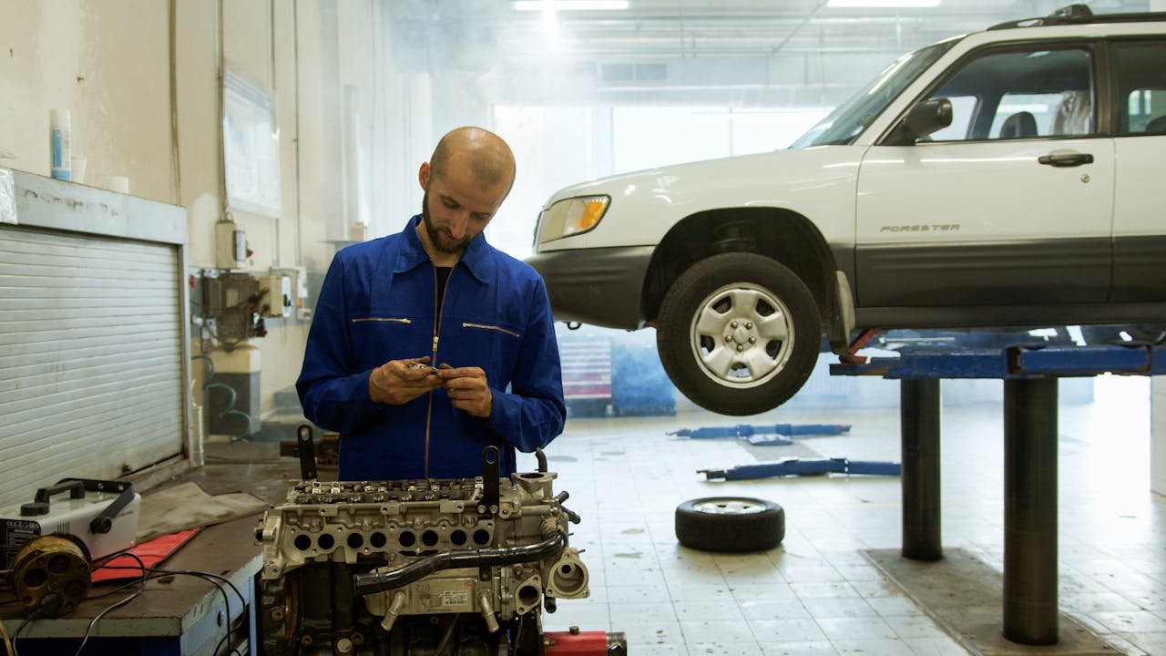 A mechanic in blue uniform inspecting an engine in a professional auto repair workshop.